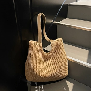 Beige woven straw tote bag with brown leather straps displayed on a modern black staircase