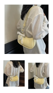 Detail of pale yellow half-moon bag featuring a lace bow and pearl pendant charm