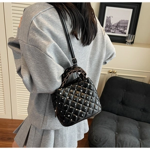 Close-up of quilted black bucket bag with silver studs and woven handle on model