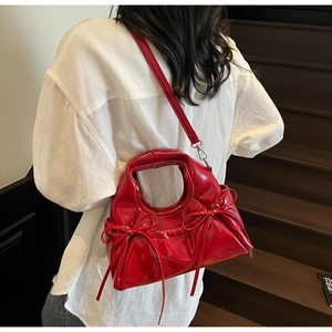 Detail of red patent leather dumpling bag with decorative bows and round handle