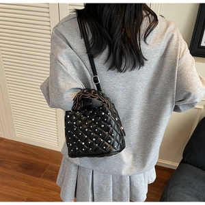 Detail of a black quilted bucket bag with rhinestones and a woven handle worn by a model