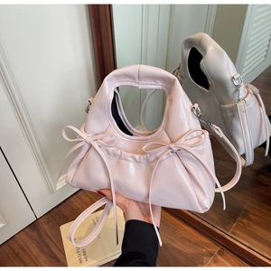 Detail of pink glossy handbag with pleated design and bows, shown with shoulder strap