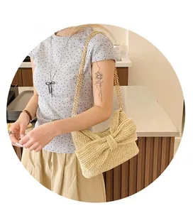 Detail of straw woven crossbody bag featuring a large decorative bow and gold metal chain