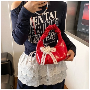 Détail du sac rouge en forme de coquillage avec breloque nœud perlé et cuir verni