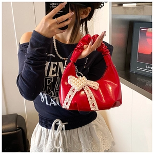 Detail of red patent leather dumpling bag featuring pearl heart and lace bow accent