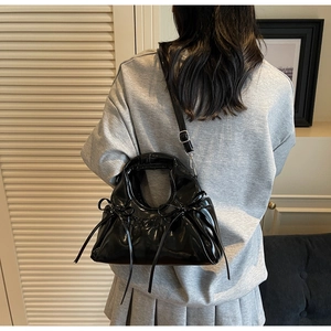Détail d'un sac en cuir verni noir avec nœuds décoratifs et bandoulière réglable