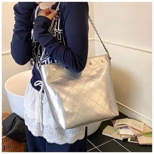 Detail of silver quilted bucket bag with chain strap shown on model in a home setting