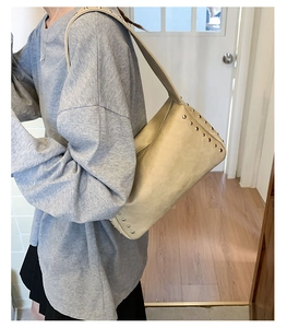 Close-up of cream shoulder bag with silver studs and wide strap on model