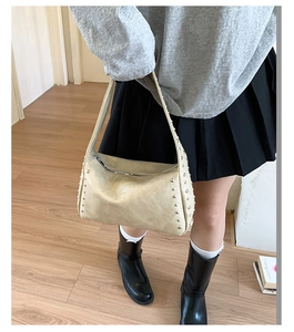 Detailed side view of beige pillow bag with silver studs worn by a female model