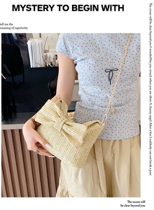 Detail of a beige straw woven crossbody bag with a large bow and gold metal chain strap