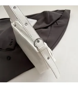 Detail of white textured shoulder bag with silver eyelets on strap over a grey blazer