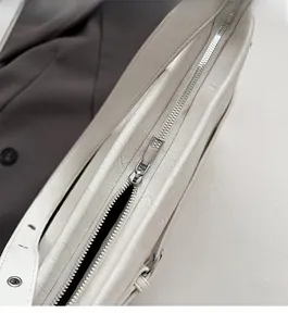 Detailed close-up of premium silver zipper and leather strap on a white underarm bag