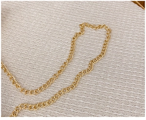 Close-up of a polished golden metal chain strap on a soft beige knit fabric background