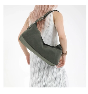 Dark green hobo shoulder bag with silver rivets worn by a model in a white dress