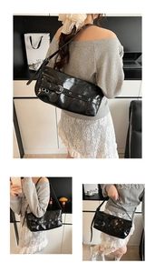 Detail of black glossy underarm bag showing silver metal eyelets and adjustable strap