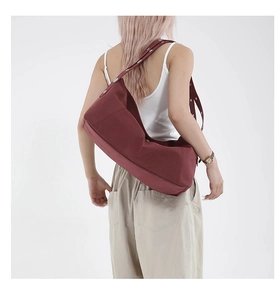 Detail of burgundy crescent bag with wide shoulder strap featuring silver metal rivets