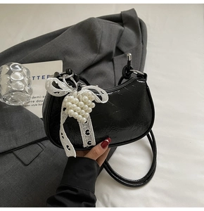Detail of black patent leather half-moon bag with lace bow and pearl heart charm