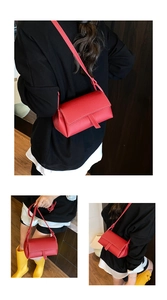 Detail view of red pebble leather pillow bag with white stitching and decorative strap