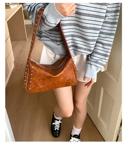 Braune Vintage-Achseltasche mit silbernen Nieten und Lederstruktur, von einem Model getragen