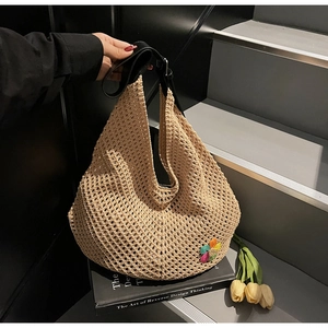 Detail of hollow-out beige tote bag with black leather handle and colorful knit flower charm