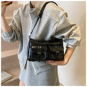 Dettaglio borsa tote nera lucida con doppie tasche anteriori e fibbie metalliche su modella