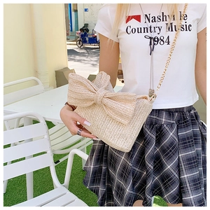 Detail of a beige straw crossbody bag featuring a large bow and gold chain strap
