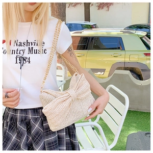 Detail of a cream straw crossbody bag featuring a large bow and gold metal chain strap