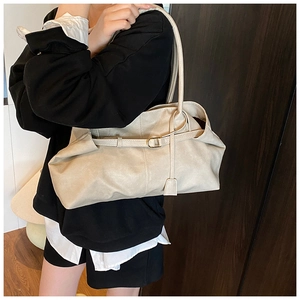 Detail of cream-colored faux leather tote bag with gold metal buckle and soft pleated texture