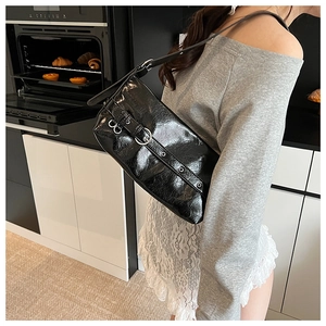 Side view of a black patent leather shoulder bag with metallic buckle and eyelet strap