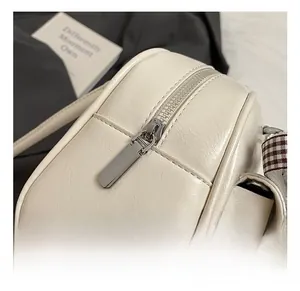 Detail view of the silver metal zipper and brown plaid strap on a cream bowling bag