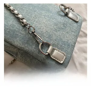 Detail of light blue denim handbag with silver D-rings and metal chain strap connectors