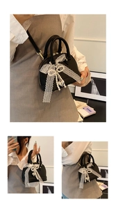 Detail of mini black shell bag with white lace bow and pearl charms for versatile carry