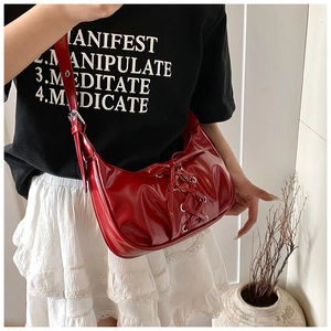 Detail of red glossy patent leather dumpling bag with decorative cross straps and shoulder strap