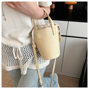 Detail of light beige bucket bag showing pebbled leather texture and drawstring closure