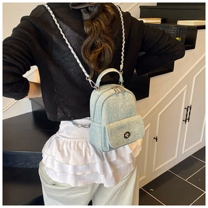 Detail of light blue denim mini backpack with silver chain straps shown on person