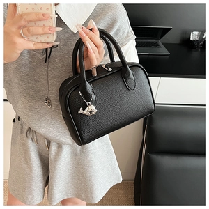 Detail of black litchi grain leather handbag featuring a cute silver whale charm and zip