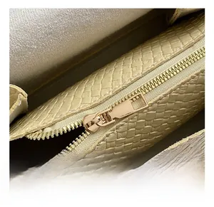 Gros plan sur la fermeture éclair dorée et la texture tissée du sac beige chic