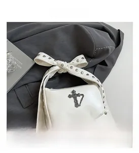 Détail d'un sac bandoulière gothique blanc avec croix en métal, chaînes et rivets argentés