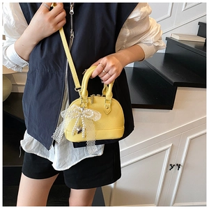 Detail of yellow shell-shaped handbag with lychee texture and pearl bow pendant