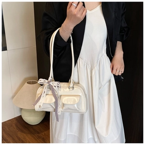 Close-up of a cream patent leather shoulder bag featuring ribbon bow and front pockets