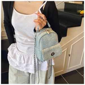 Detail of light blue denim mini backpack with silver chain strap and metallic buckle closure