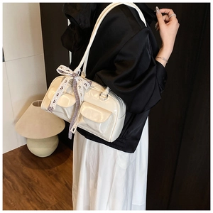 Detail of creamy white faux leather shoulder bag featuring ribbon and silver hardware