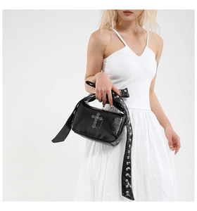 Close-up of black glossy crossbody bag featuring vintage metal cross and eyelet strap