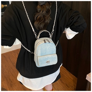 Detail of light blue denim fabric backpack with silver metal chain straps on model
