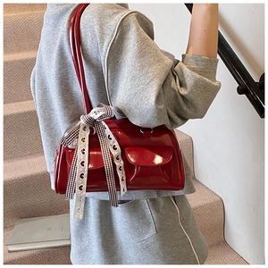 Detail of red patent leather Boston bag featuring front flap pockets and a checkered bow ribbon
