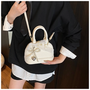 Detail of white shell handbag with lace bow, pearl charm, and heart pendant accessory