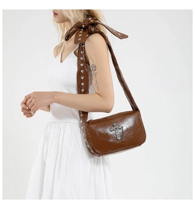 Détail d'un sac à bandoulière gothique marron brillant avec croix argentée et rivets