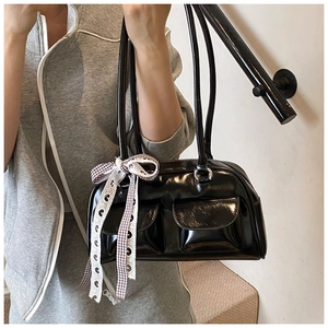 Close-up of black glossy pillow bag featuring front pockets and decorative ribbon bow