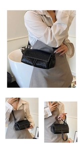 Detail of black woven crossbody bag featuring a magnetic flap and slim shoulder strap