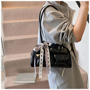Detail of black glossy PU shoulder bag with decorative bow and side pockets on stairs
